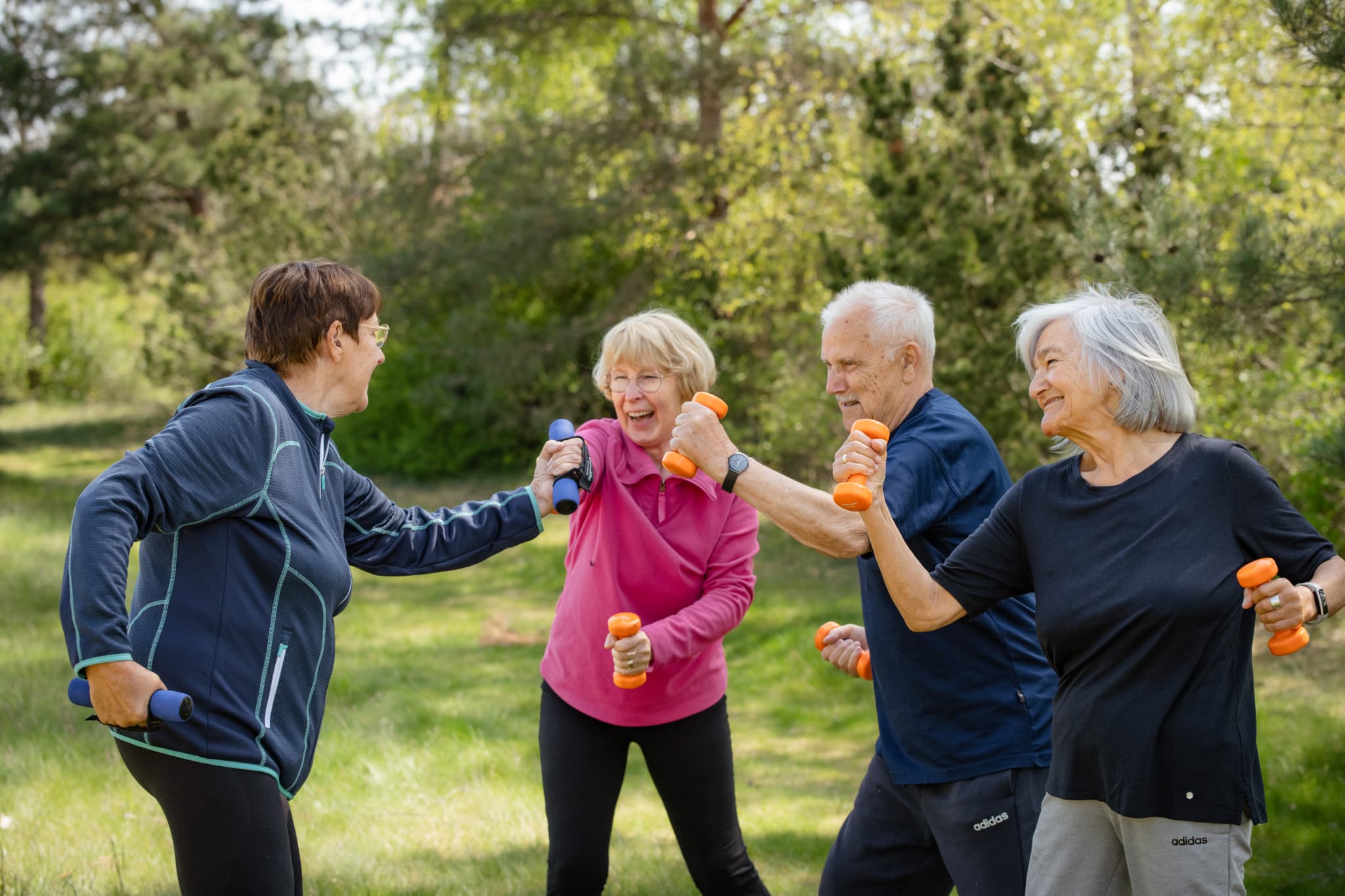 Ältere Menschen trainieren lachend mit Hanteln im Grünen in einer fröhlichen Gruppe.