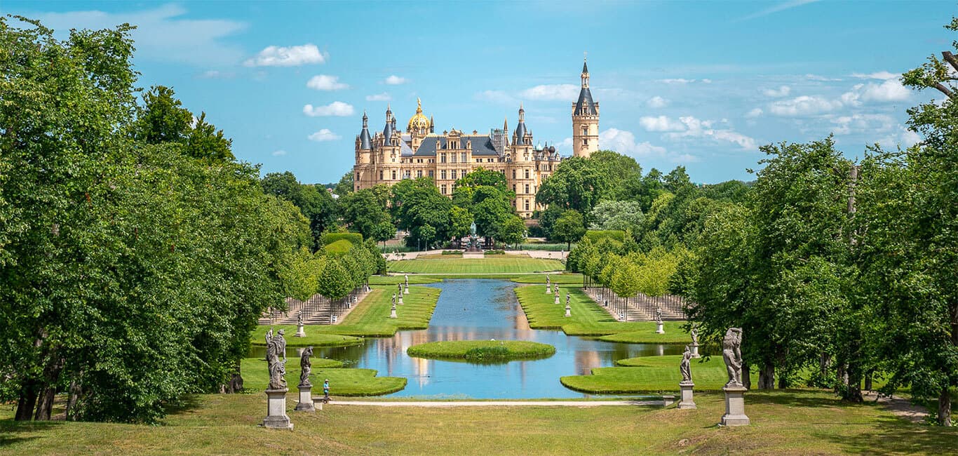 Schweriner Schloss im Sommer mit Park und Wasserbecken im Vordergrund.