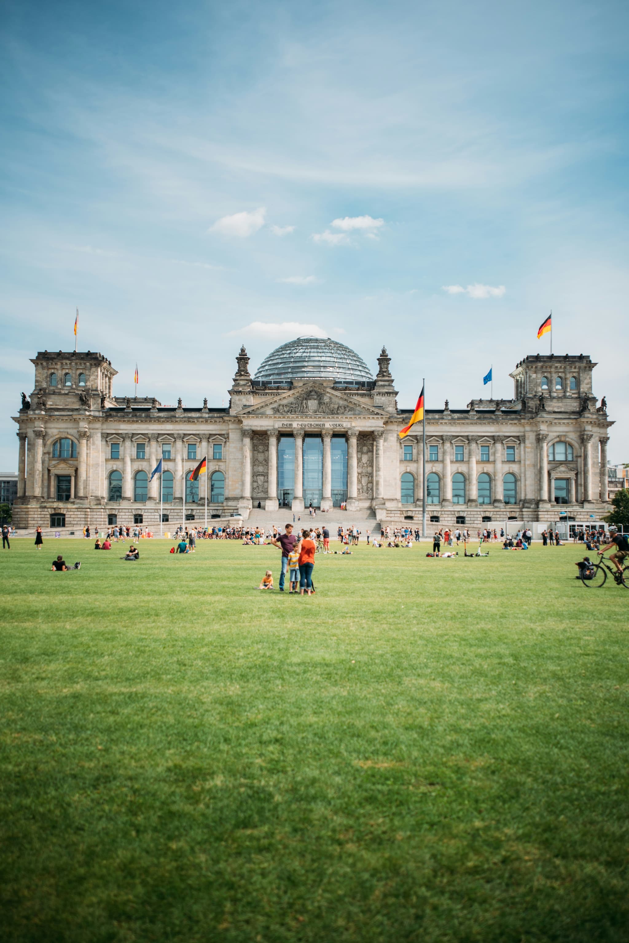 Reichstagsgebäude Berlin mit Glaskuppel und Menschen auf der Wiese.